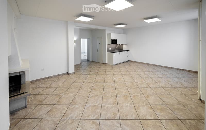 Empty room with tiled floor, white walls, and a small kitchen area featuring white cabinets, a sink, and a microwave. A fireplace is visible on the left side.