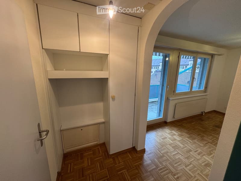 Empty room with wooden flooring, white walls, built-in cabinetry, and a large window with a view of the outside.