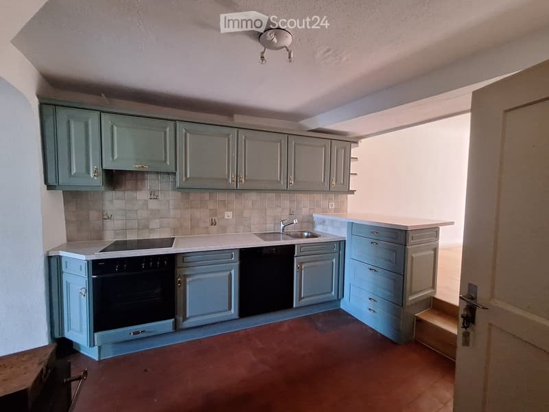 Modern kitchen with grey cabinets, white countertops, and a built-in oven. Features a sink with a modern faucet and a tiled backsplash.