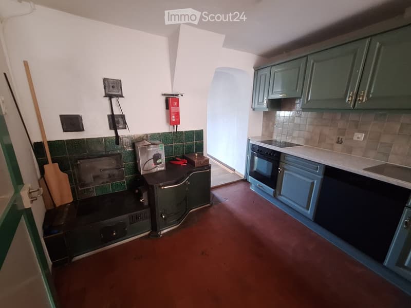 The kitchen features green cabinets, a white countertop, and a stove with an oven. There is a tiled backsplash and a wooden floor.