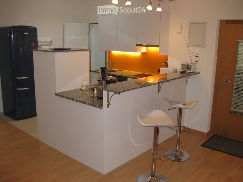 Modern kitchen with white cabinets, granite countertop, stainless steel appliances, and two white bar stools.