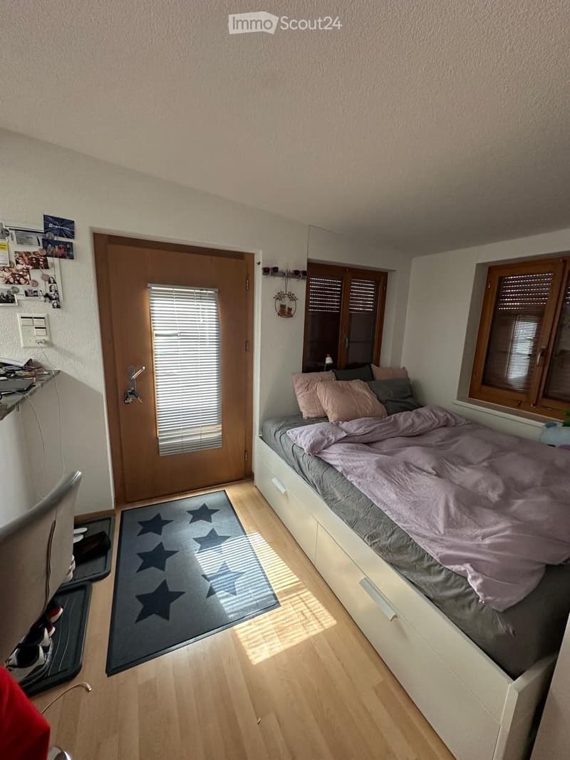 Cozy bedroom with a single bed, pillows, a small desk, a chair, and a rug with star patterns on the floor.