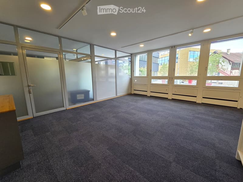 Empty room with carpeted floor, large windows, glass partitions, and recessed lighting.