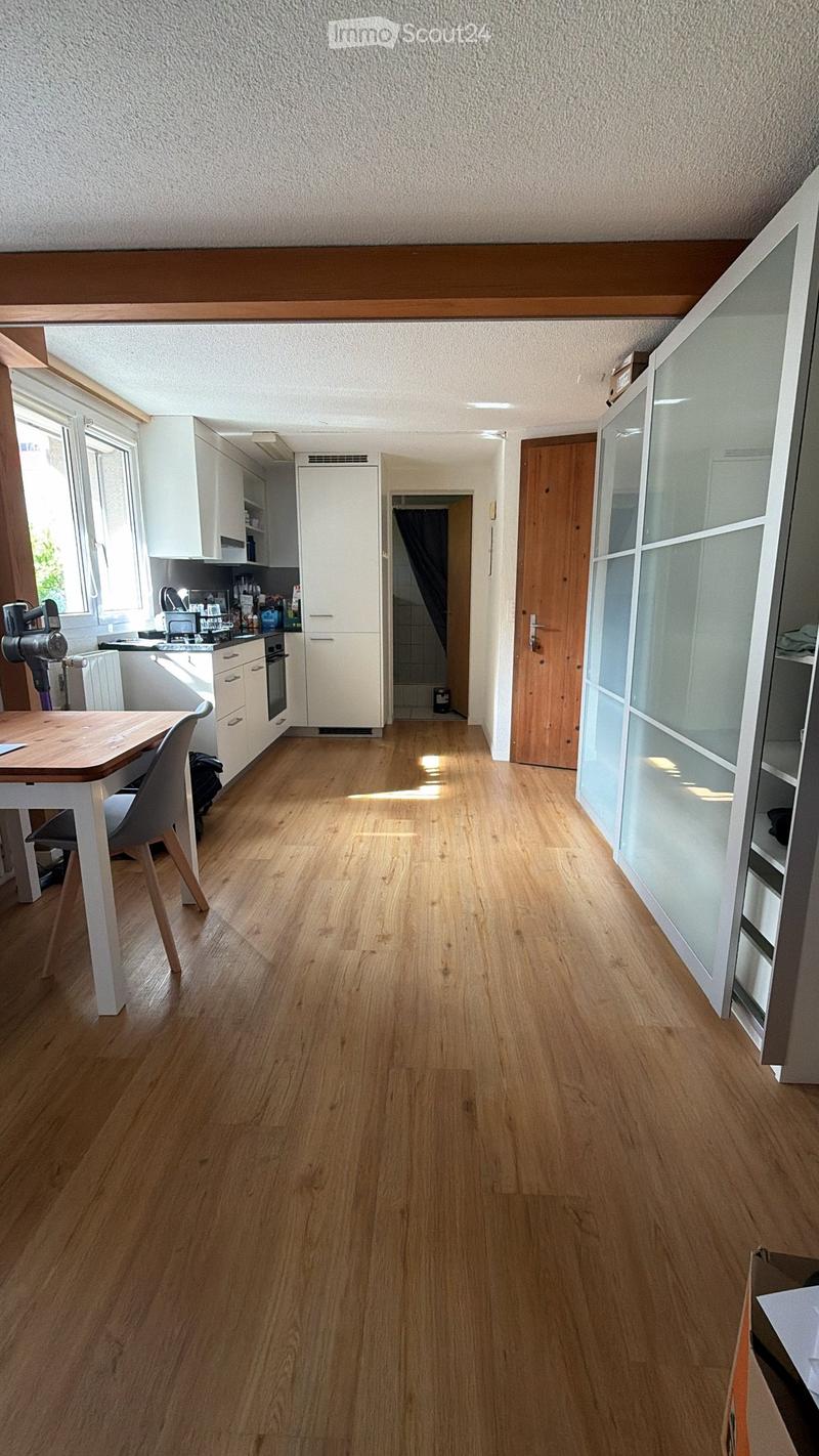 Bright kitchen with light wooden flooring, white cabinets, a small dining area with a table and chair, and a visible oven and faucet.