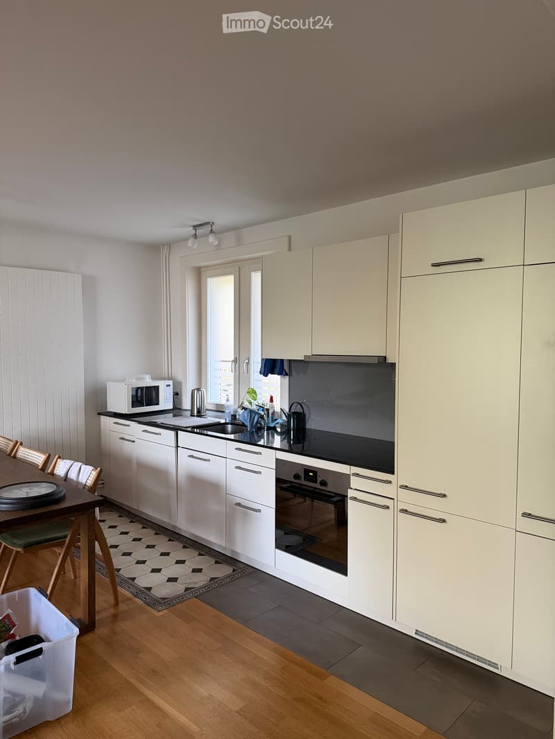 Modern kitchen with white cabinets, black countertop, microwave, oven, sink, and small dining area with a table and chairs.