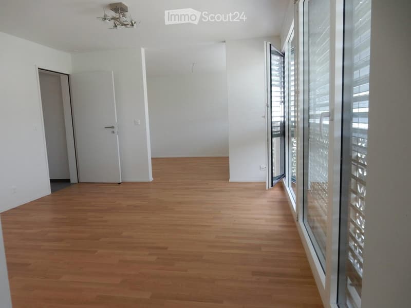 Empty room with light wooden flooring, white walls, and large glass windows with blinds. No furniture or equipment present.