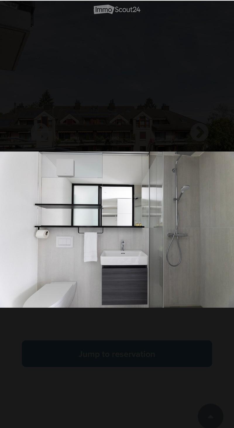 Modern bathroom with a white toilet, sink, mirror, and glass-enclosed shower. Features a towel, toilet paper, and a sleek cabinet.