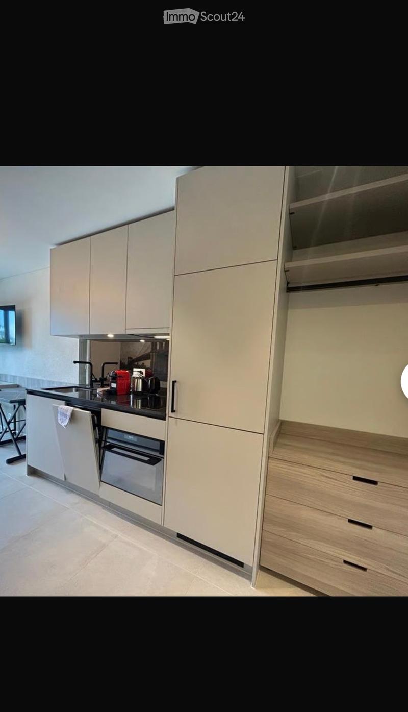 Modern kitchen with light-colored cabinets, a black countertop, and stainless steel appliances including a sink, oven, and faucet.