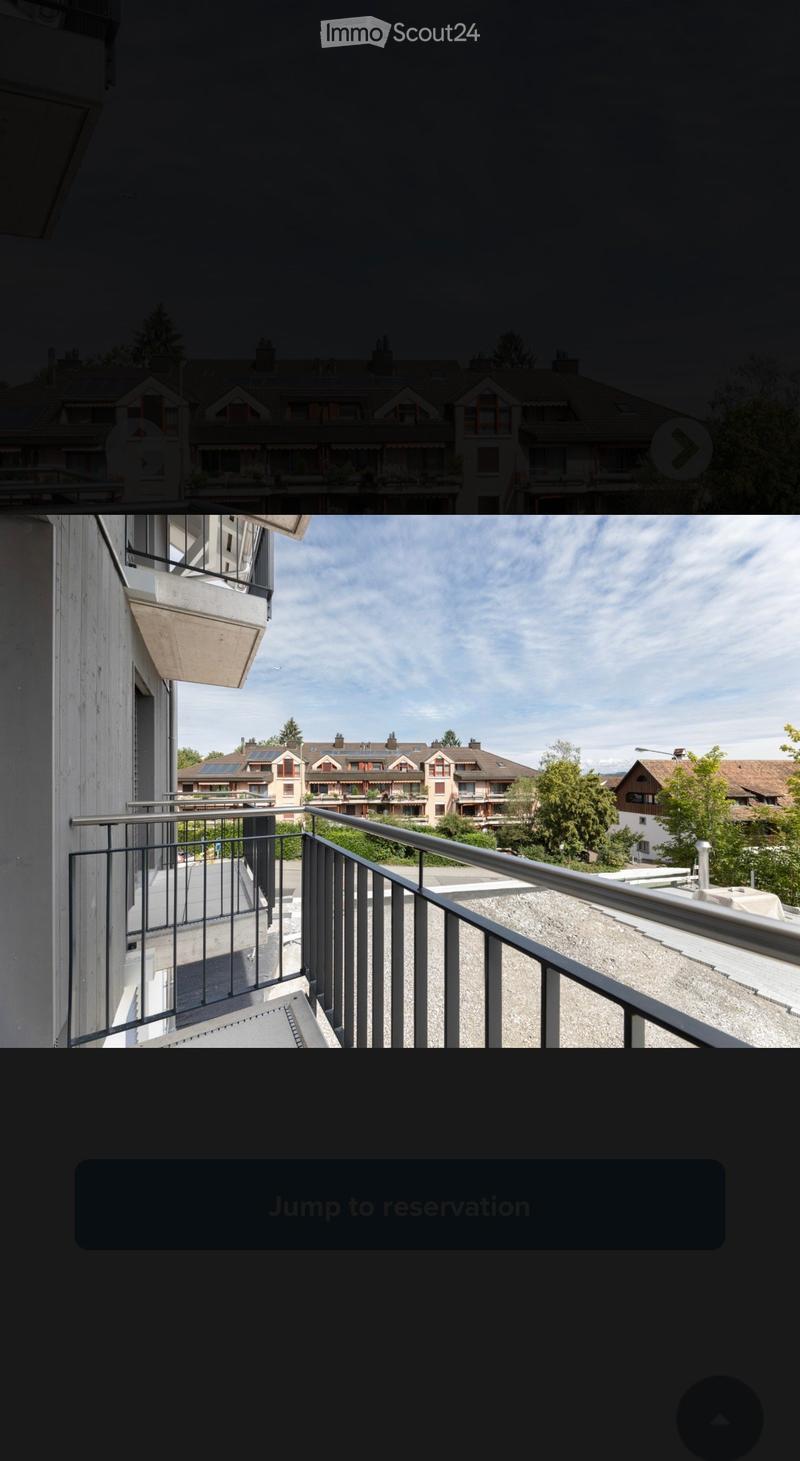 Balcony with metal railing, overlooking a residential area with multiple buildings and greenery.