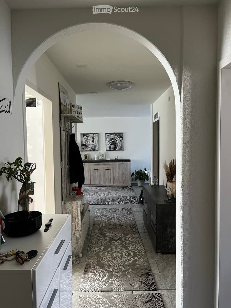 A modern hallway with arched ceiling, patterned rugs, and decorative items on side tables.