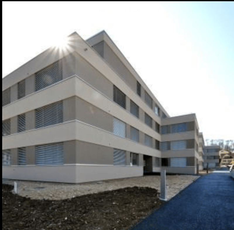 Modern multi-story building with a clean, contemporary design, featuring large windows and a symmetrical facade.