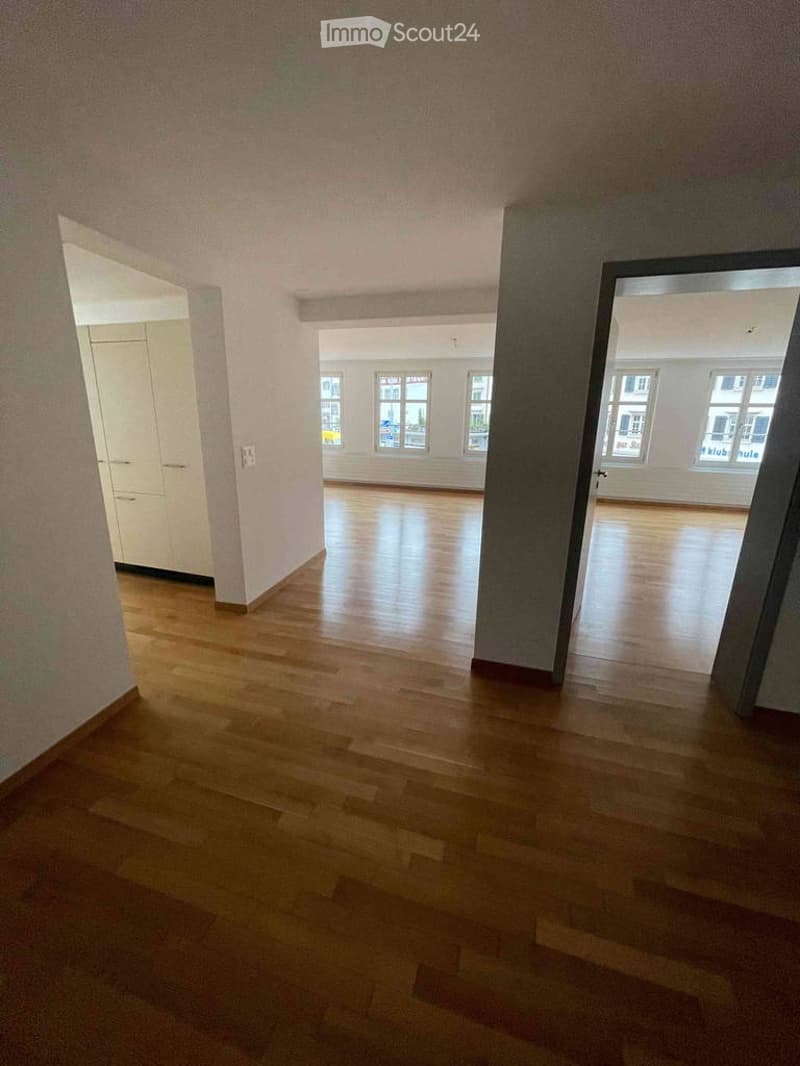 Empty hallway with wooden flooring, white walls, and multiple doors leading to other rooms.