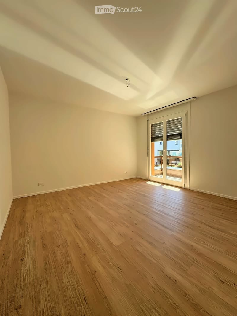 Empty room with light wooden flooring and white walls, featuring a large sliding glass door leading to a balcony.