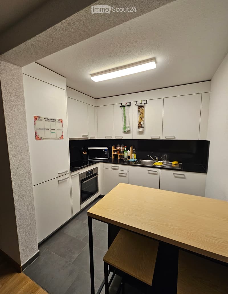 Modern kitchen with white cabinets, stainless steel appliances, and a wooden island. Features include a refrigerator, oven, microwave, sink, and a small wooden stool.