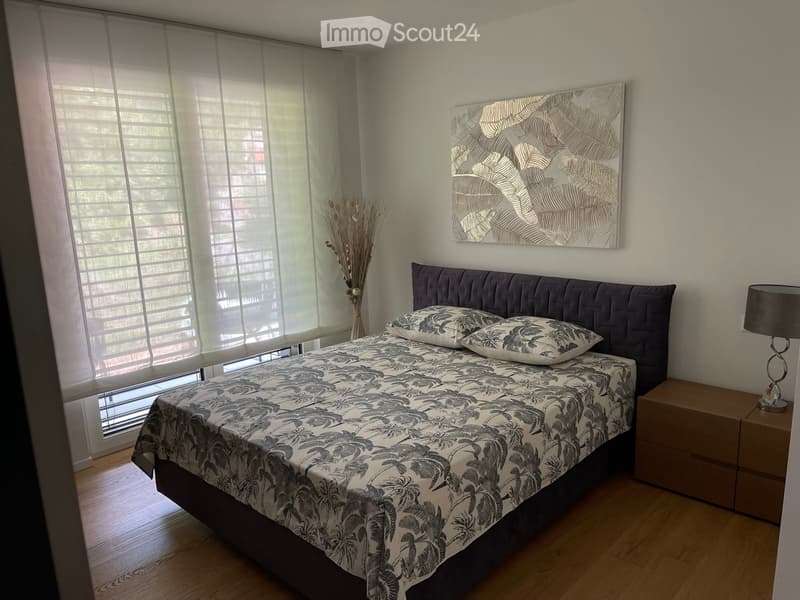 Modern bedroom with a large bed, patterned bedspread, nightstand, lamp, and decorative wall art.