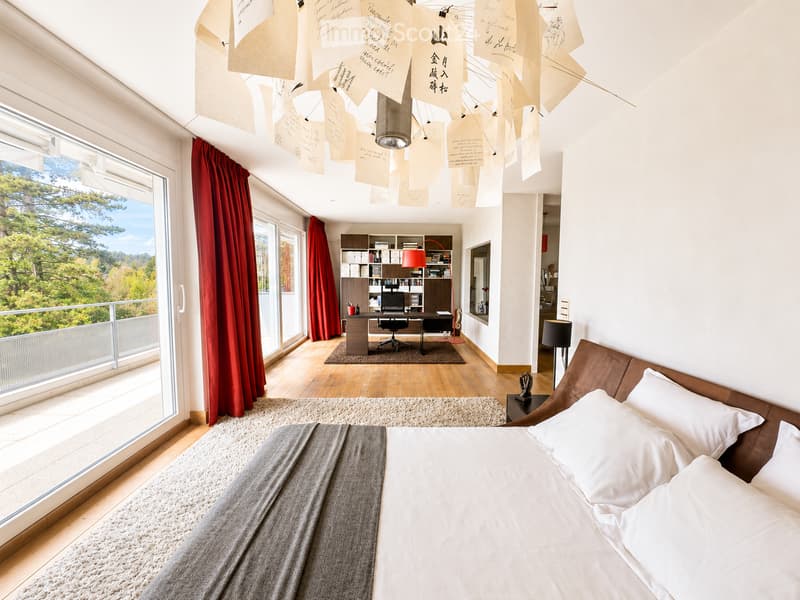 Modern bedroom with a large bed, wooden desk, bookshelf, and large windows offering a scenic view.