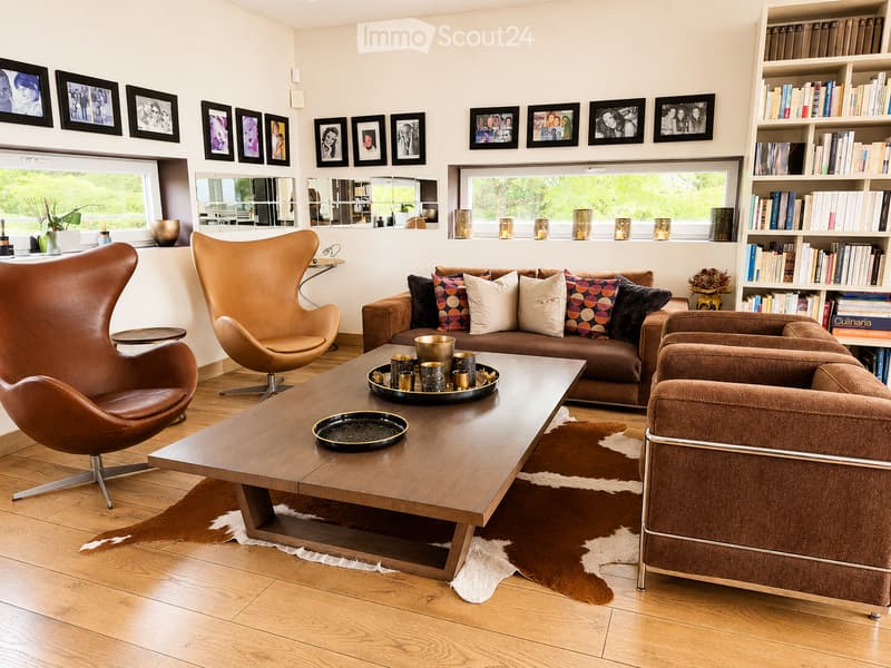 Modern living room with a brown leather sofa, two leather armchairs, a wooden coffee table, a bookshelf, and decorative mirrors on the wall.