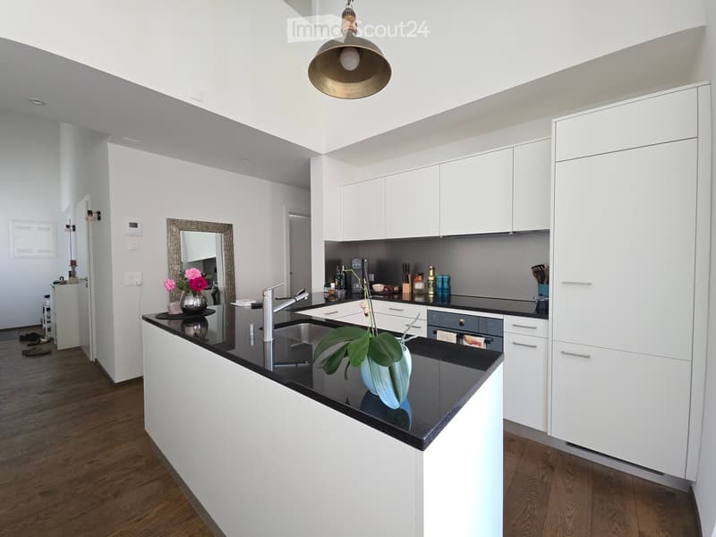 Modern kitchen with white cabinets, black countertops, a central island, and a hanging pendant light. Features a sink, faucet, and decorative vases on the counter.