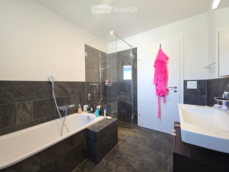 Modern bathroom with a bathtub, glass-enclosed shower, sink, and towel hanging on the door.