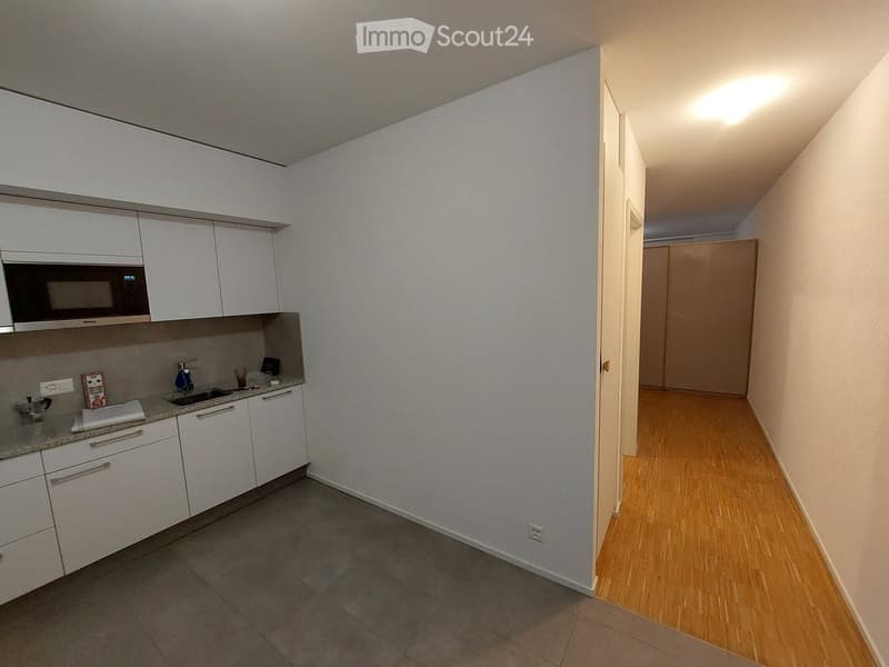 A modern kitchen with white cabinets, a microwave, a sink, and a small hallway leading to another room.