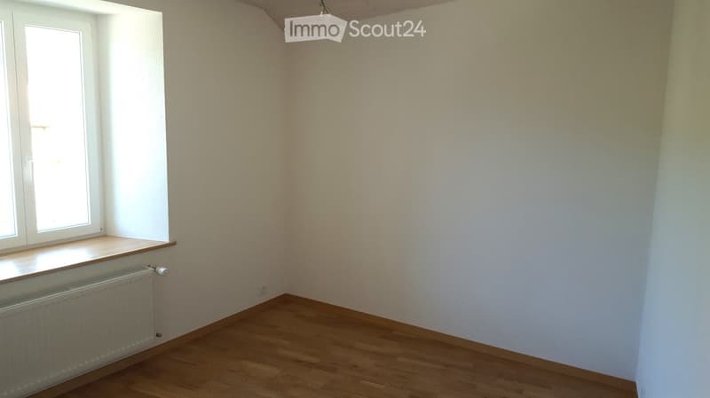 Empty room with wooden flooring, white walls, and a window with a radiator below it.