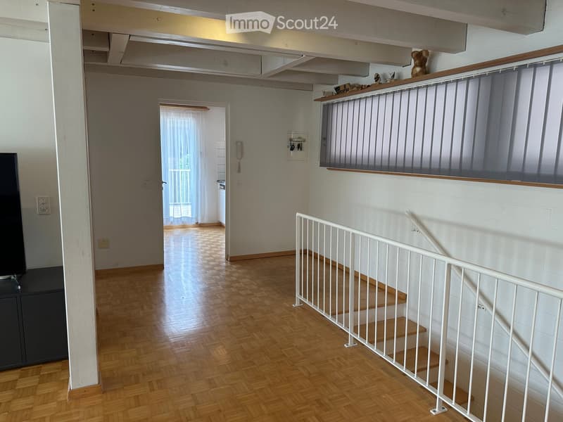 Hallway with wooden flooring, white walls, staircase with white railing, and a small balcony area with a teddy bear on the railing.