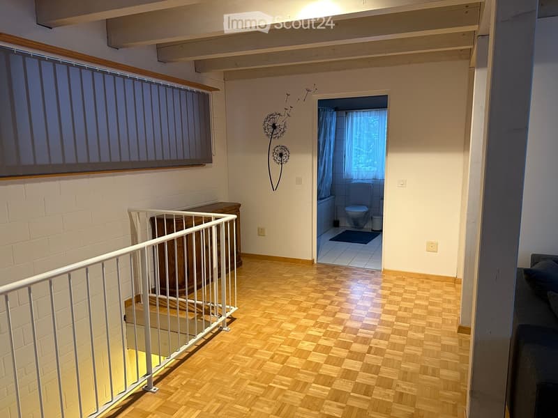 Hallway with wooden flooring, white railing, and a view into a small bathroom with a toilet and bathtub.