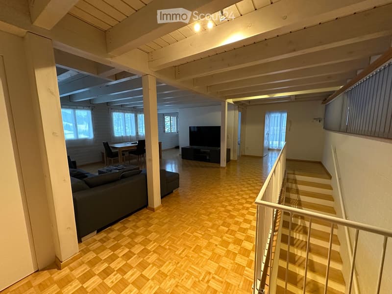 Open-plan living and dining area with wooden flooring, a staircase leading to another level, and modern furnishings including a sofa, coffee table, TV, and dining set.