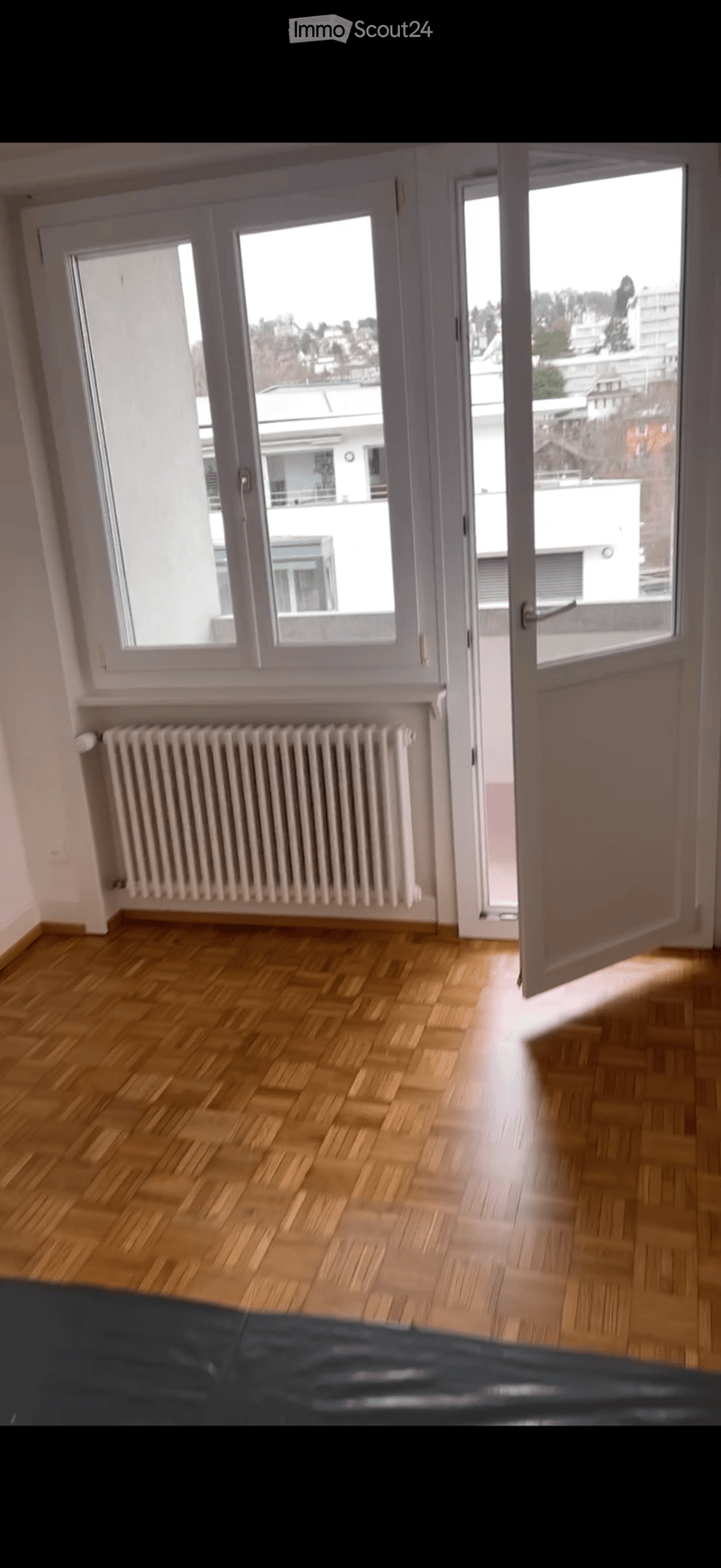 Empty room with wooden flooring, white walls, large windows, and a radiator. No furniture or equipment present.