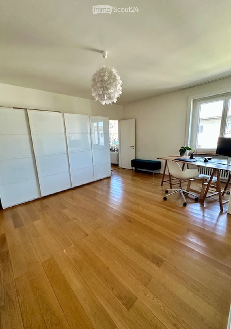 Empty room with light wooden flooring, white walls, large white closet units, and a hanging decorative light fixture.