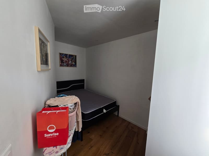 A small bedroom with a bed, a shopping bag, and a handbag on a changing table, along with picture frames on the wall.