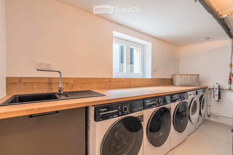Modern bathroom with a wooden countertop, sink, faucet, and multiple washing machines and a dishwasher installed below the counter.