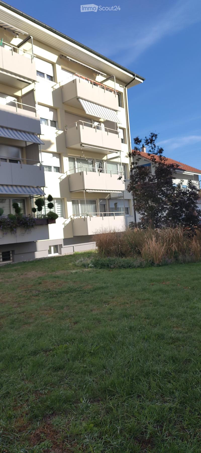 Multi-story residential building with balconies, raised ground floor, and surrounding greenery.