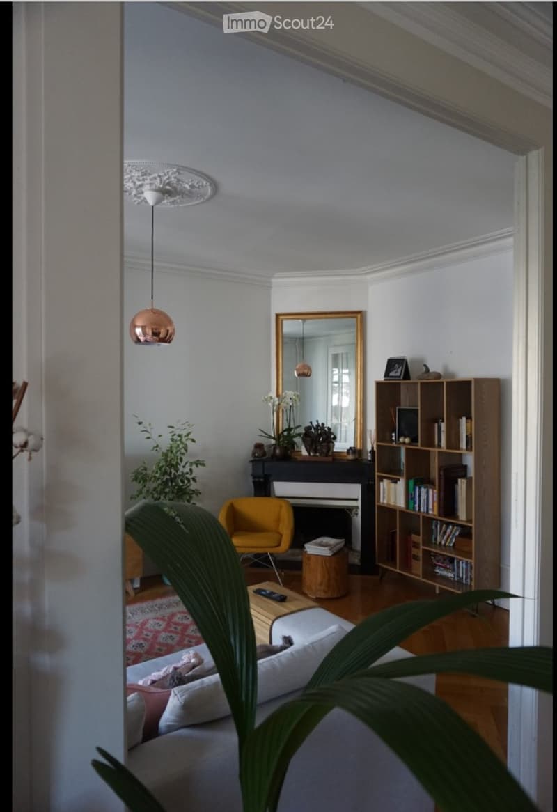 Living room with a white sofa, coffee table, yellow armchair, bookshelf, mirror, piano, and decorative plants.