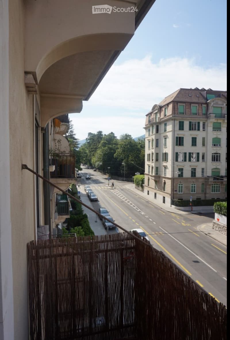 Balcony overlooking a street with cars, buildings, and greenery in the background.
