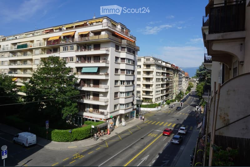 Multi-story residential building with balconies and awnings, located on a street with traffic and pedestrians.