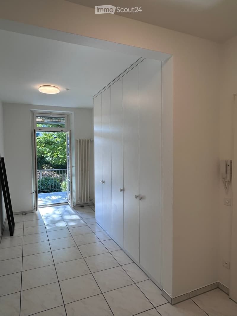 Empty hallway with white walls, tiled floor, built-in white closet, and a sliding glass door leading to a balcony area.