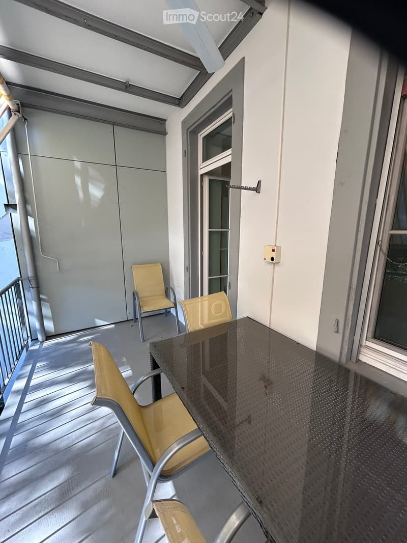 Balcony with a table and three chairs, metal railing, and a door leading inside.
