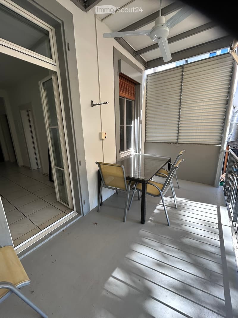 Balcony with a glass table and two yellow chairs, a ceiling fan, and a sliding glass door leading to the interior.