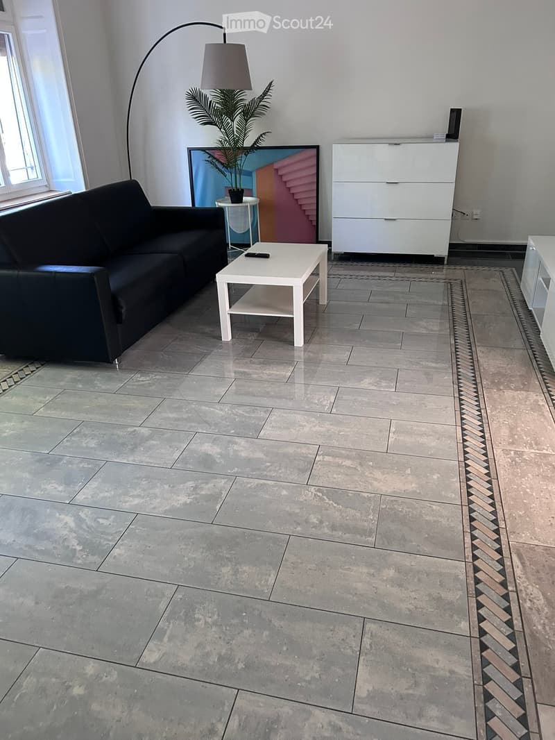 Modern living room with a grey sofa, white coffee table, floor lamp, potted plant, and a white cabinet.