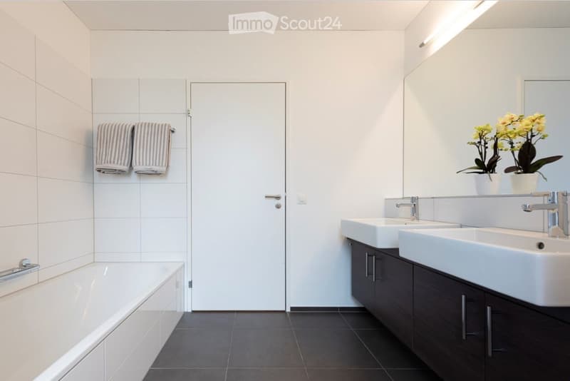 Modern bathroom with white tiles, a bathtub, double sink vanity with dark wood cabinets, a large mirror, and decorative flowers on the counter.