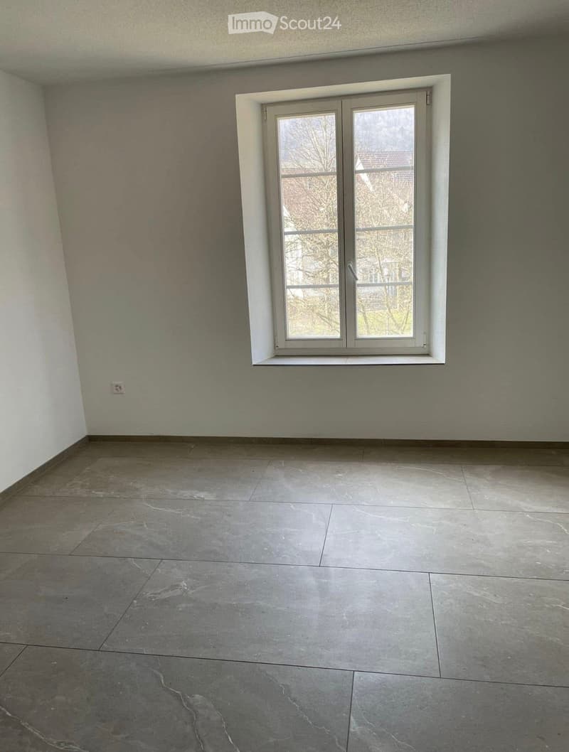 Empty room with grey tiled floor and white walls, featuring a single window with white frame and glass panels.