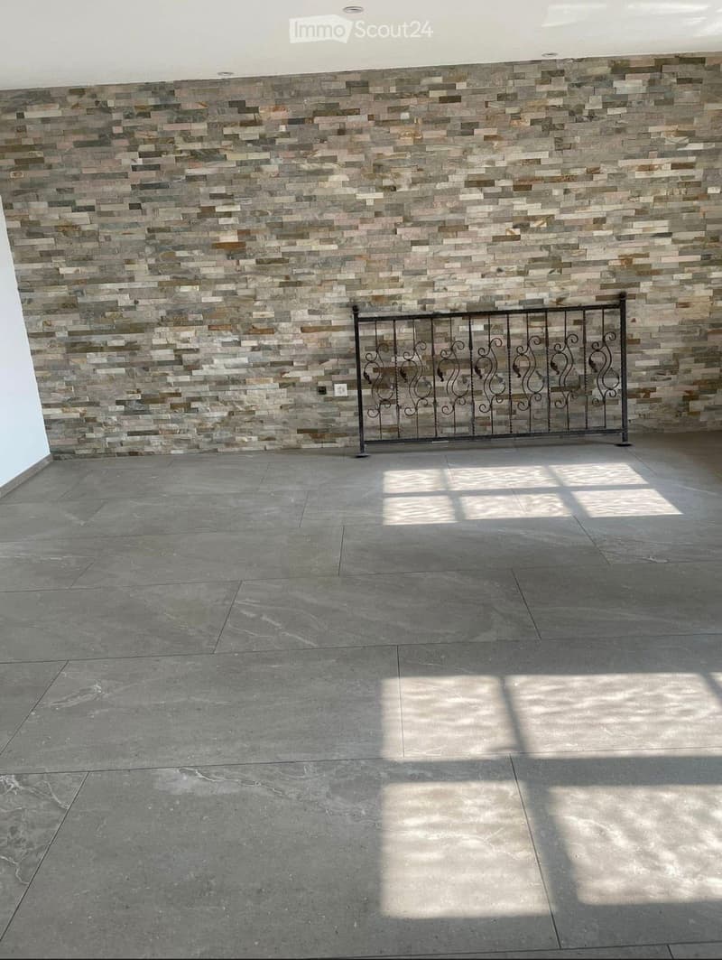 Empty room with a tiled wall and a decorative metal gate, featuring a concrete floor and natural light from an unseen source.