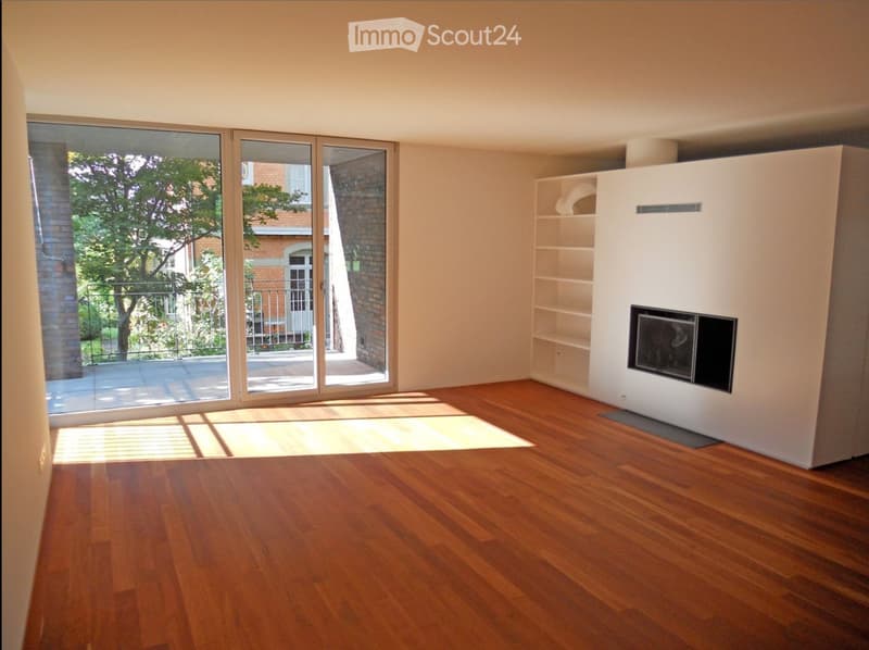 Empty room with wooden flooring, large sliding glass doors leading to a balcony, and a built-in fireplace unit with shelves.