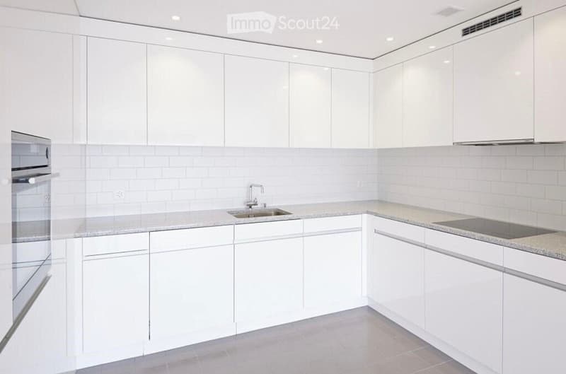 Modern kitchen with white cabinets, granite countertops, a sink with a modern faucet, and an oven. The walls are tiled in light gray, and the floor is tiled in a neutral tone.