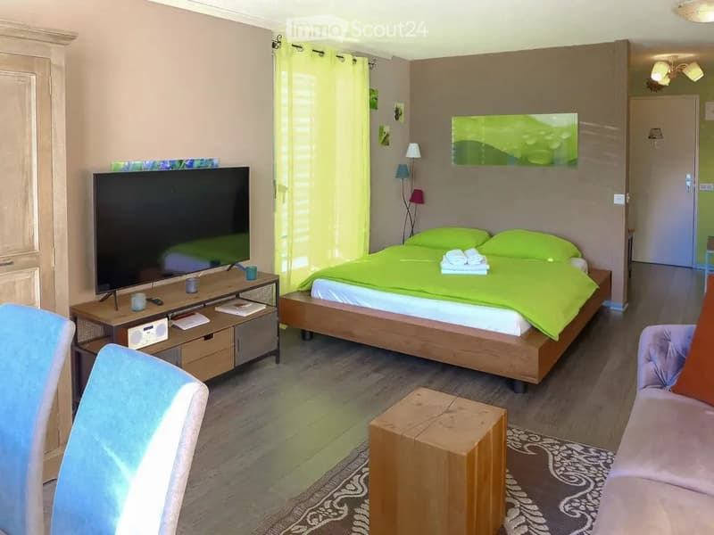A cozy bedroom with a double bed, nightstand, small table, chair, sofa, mirror, and decorative items.