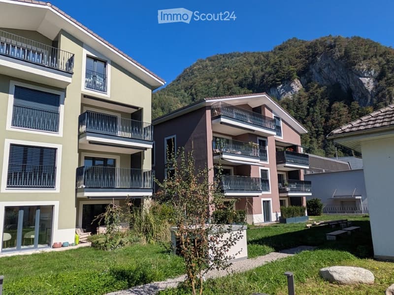 Modern multi-story residential building with balconies overlooking a green lawn and mountain view.