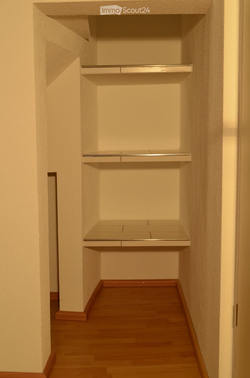 Empty closet with built-in shelves and drawers, light-colored walls, and wooden flooring.