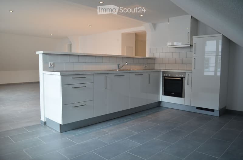 Modern kitchen with grey cabinets, a central island, a sink with a faucet, an oven, and a refrigerator. The floor is tiled in dark grey, and the walls are white with grey tiles around the sink area.