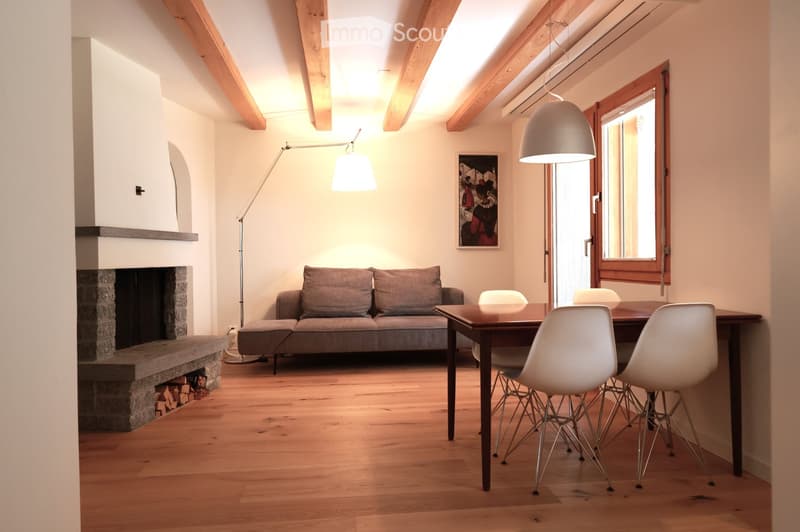 Living room with exposed wooden beams, fireplace, sofa, dining table with chairs, and modern floor lamps.